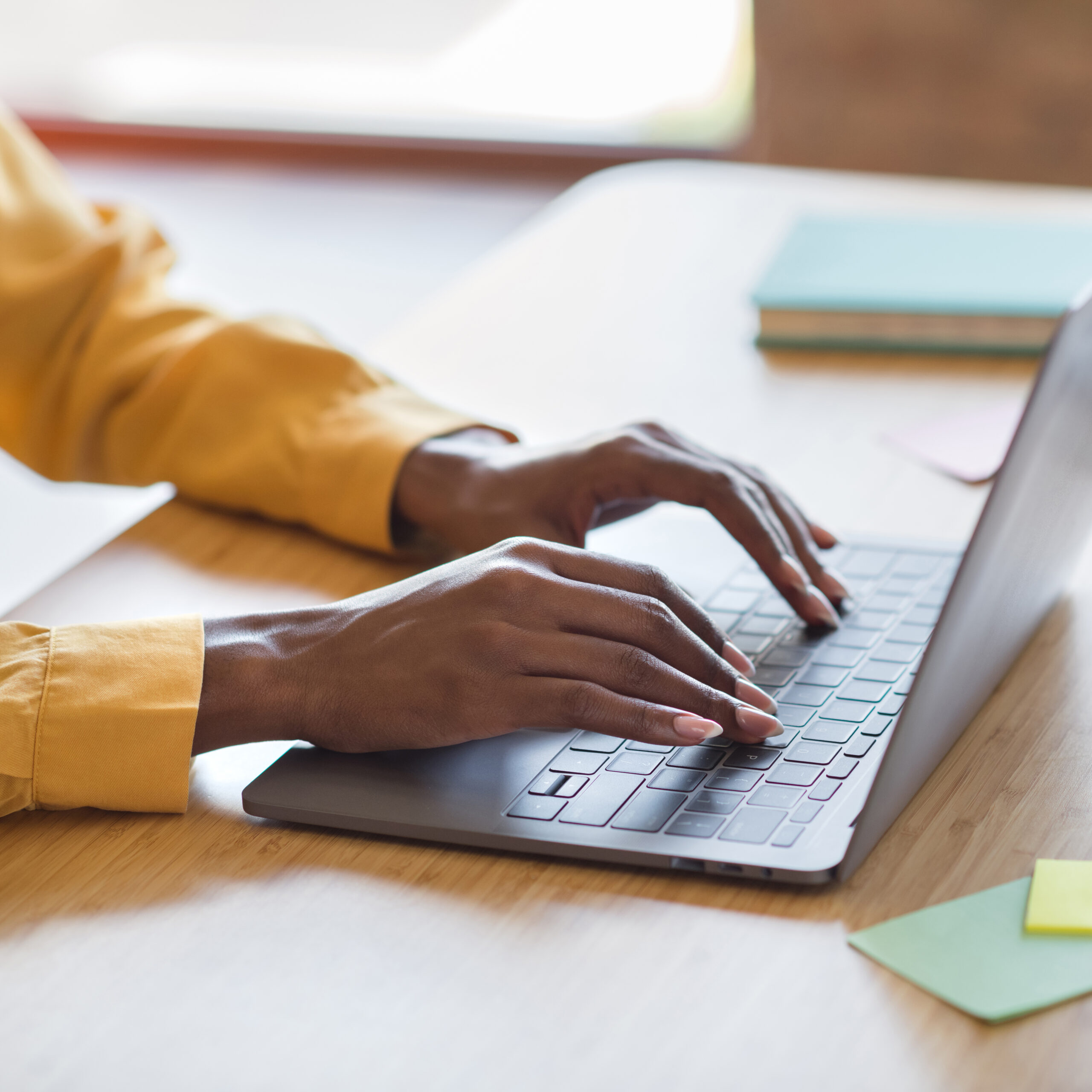 Cropped,Photo,Portrait,Of,African,American,Woman's,Hands,Typing,On Two hands type at a laptop sitting on a table.