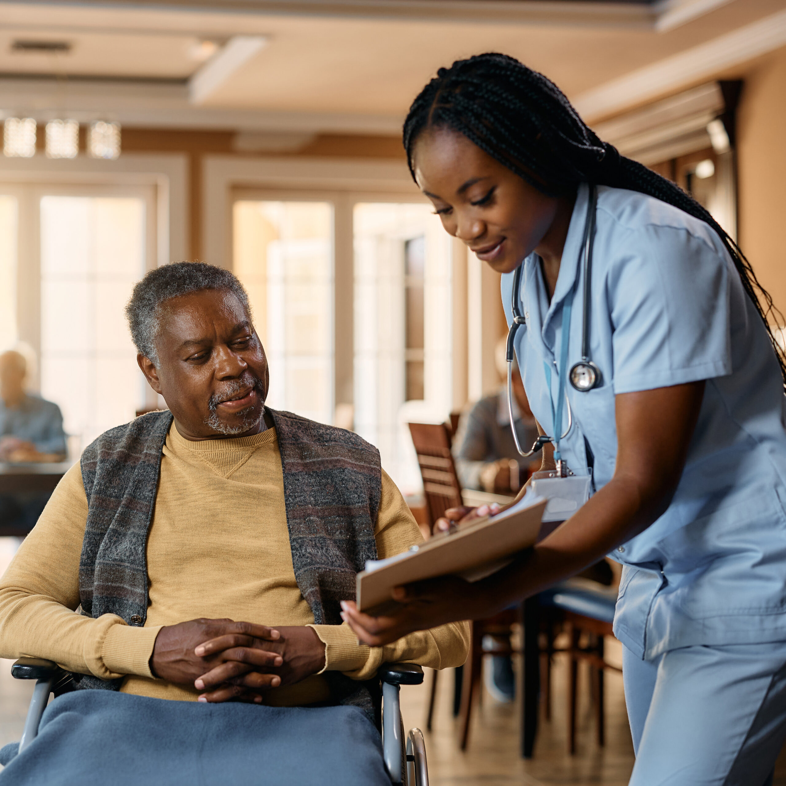 Senior black man in wheelchair and young nurse analyzing medical paperwork at nursing home. a black female nurse shows a senior black male patient something on a clipboard